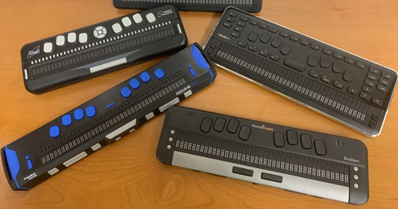 A variety of braille keyboards for computer, including wired and wireless models, displayed on a desk for comparison