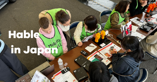 Group at a table demonstrating Hable devices in Japan, with "Mobility for ALL" vests and materials visible.