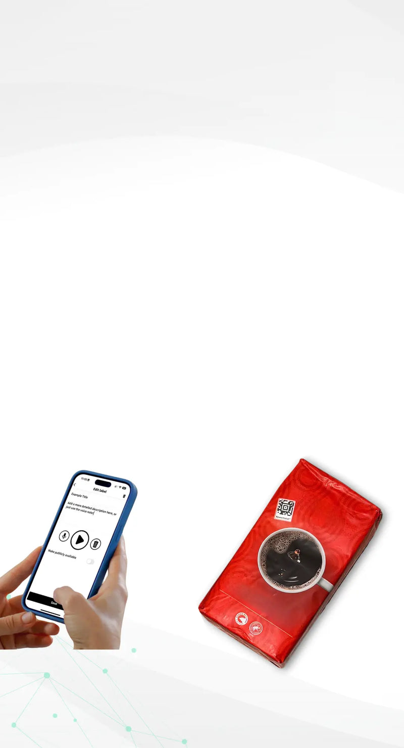 On a clean white background, a pair of hands holds a smartphone displaying the Speechlabel app in editing mode. The screen shows options to record or play an audio message and to save the label. On the right side lies a red package of coffee with a white cup of black coffee printed on it. At the top of the package is a square black-and-white Speechlabel grocery sticker with a red border, clearly visible.