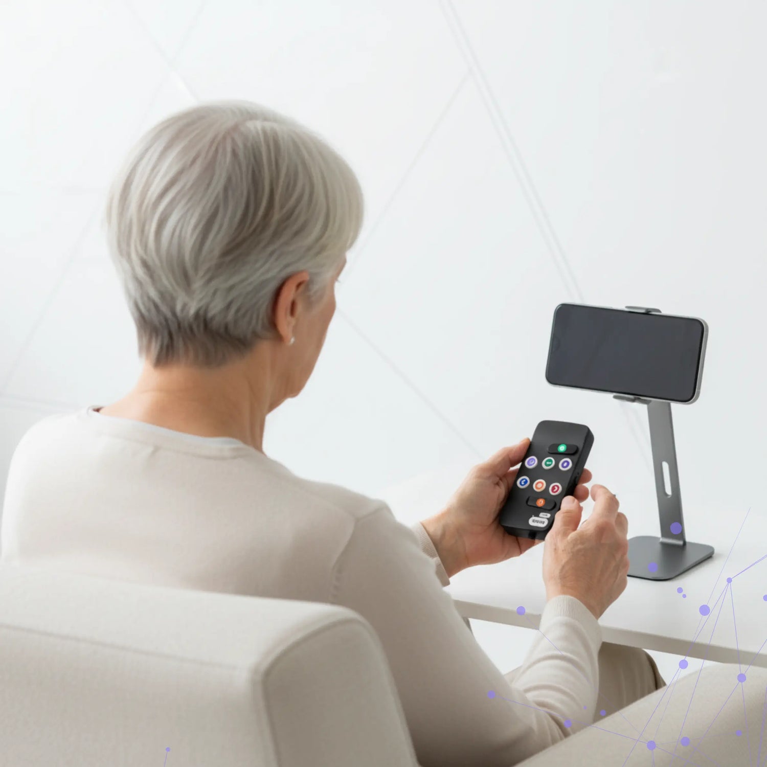An older woman sits on a chair using a Hable Easy device to control her smartphone, which is placed on a stand in front of her. The setup demonstrates how the Hable Easy enables easy phone control for blind and visually impaired users.