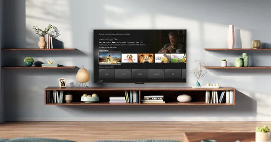 A modern living room with floating shelves and a wall-mounted TV displaying a movie selection screen. The shelves hold books, vases, and small decorative items