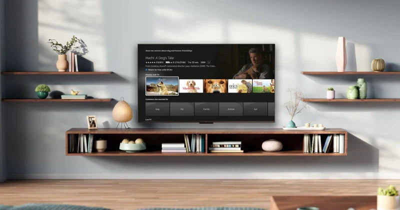 A modern living room with floating shelves and a wall-mounted TV displaying a movie selection screen. The shelves hold books, vases, and small decorative items