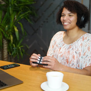 Woman holding the Hable One in two hands, with the buttons facing away from here. Which is the correct way to hold the Hable One. Sitting in an office setting in front of a desk.