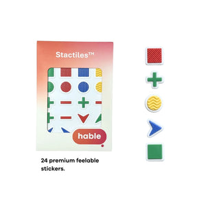 The Hable Stactiles Basic Shapes retail box is shown next to five individual sample stickers arranged vertically: a red square with a cross-hatch texture, a green plus sign, a yellow circle with a wavy pattern, a blue chevron with a pebble texture, and a smooth green square. Text at the bottom states: "24 premium feelable stickers."