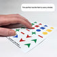 A close-up, angled photograph of a hand scanning a sheet of basic shape stickers. The focus is on the diverse surface textures: a red square with a grid pattern, a blue circle with vertical ridges, and a yellow circle with a wavy embossed surface. These textures provide additional tactile cues beyond the outer shape. Text at the bottom reads: "The perfect tactile feel to every sticker."