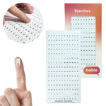 A composite image featuring the Hable Stactiles 180-count Braille sticker set. A circular inset shows fingers scanning across a dense sheet of small white stickers. A single sticker with the letter "H" and its Braille dots is shown on a fingertip for size comparison. The background displays the full sheet, organized alphabetically with multiple copies of each letter and punctuation marks, next to the retail packaging.