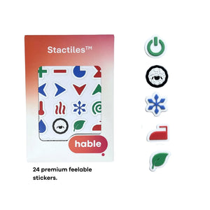 The Stactiles Washing retail box is shown next to five individual sample stickers arranged vertically: a green power icon, a black-and-white sheep (wool), a blue snowflake (delicates/cold), a red iron (synthetic/ironing), and a green leaf (eco-mode). Text at the bottom indicates there are "24 premium feelable stickers" in the set.