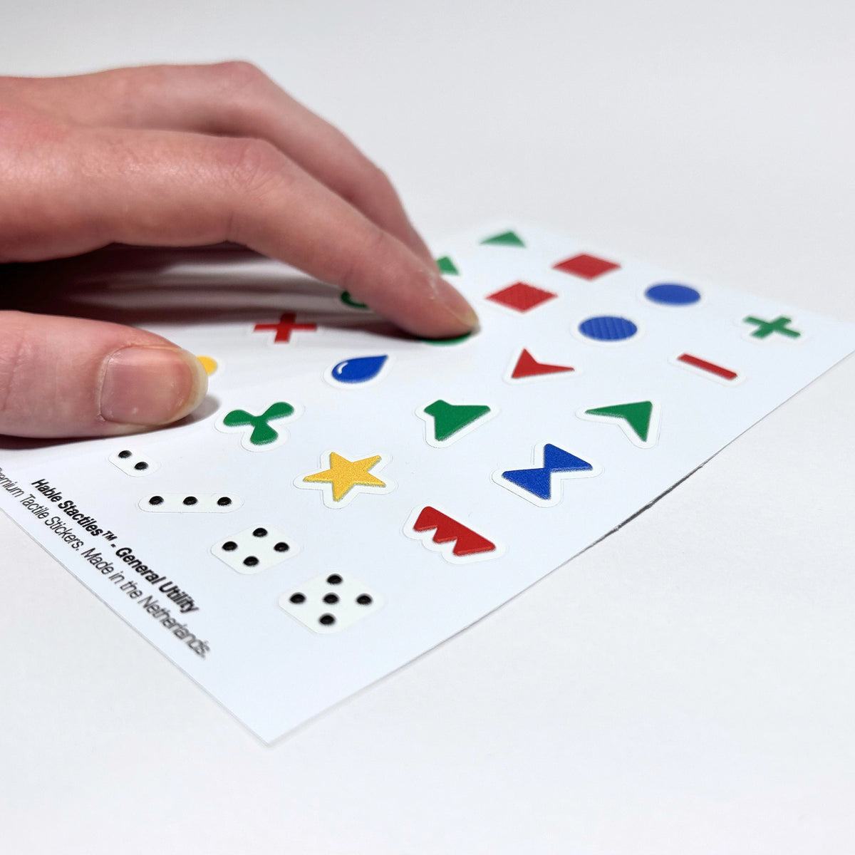 Close-up photo of an index finger feeling the raised appliance control symbols on the "Hable Stactiles - General Utility" sticker sheet.