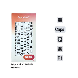 The Stactiles retail box is displayed next to five individual sample stickers arranged vertically: a Windows logo, a "Caps" key, the letter "Q", an Apple Command symbol, and the "F1" key. Each sticker features bold black text or symbols on a white background with a raised 3D texture. Text at the bottom reads: "80 premium feelable stickers."