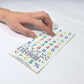 Close-up perspective photo of a hand resting an index finger on the "Hable Stactiles - Numbers" sticker sheet, demonstrating the tactile feel of the raised colorful numbers and math symbols on a smooth white surface.