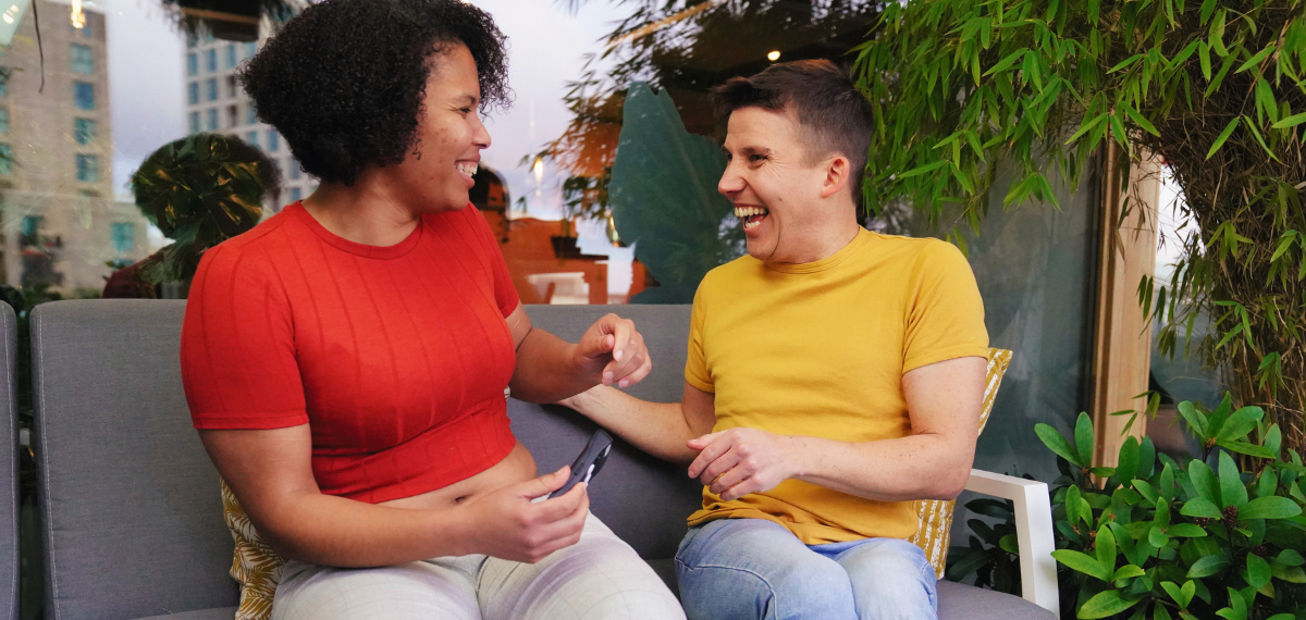 Two people sitting on a couch outdoors,  laughing and having fun, holding the Hable One Braille keyboard.