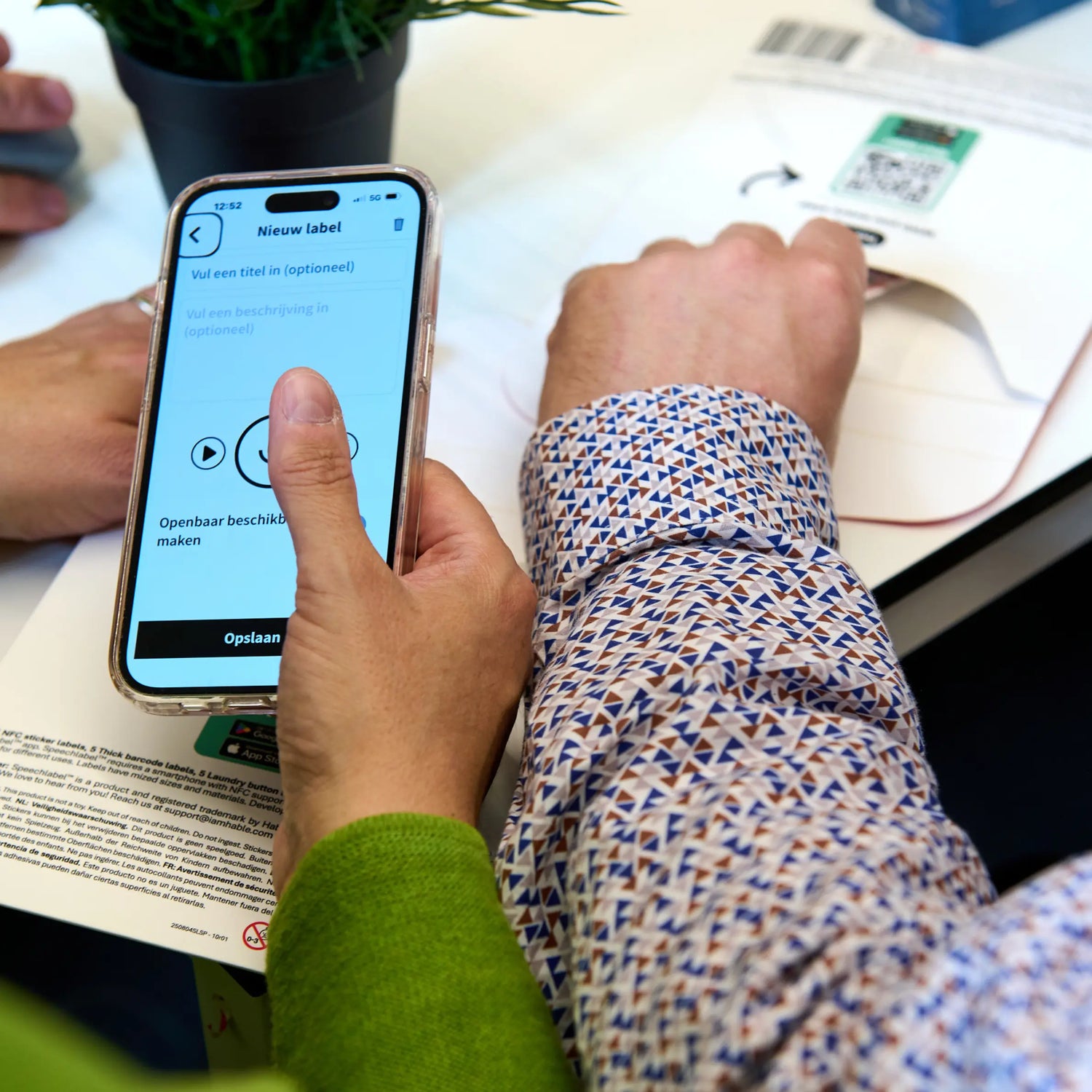 Close-up of two people holding a smartphone displaying the Speechlabel app. The screen shows the 'New Label' interface with the specific option to 'Make publicly available,' demonstrating how to share label information with others."