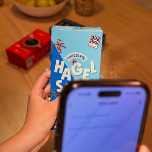 Person holding a blue box with dutch breakfast, on it there is a grocery Speechlabel label. In the front there is a phone with the Speechlabel app scanning this product.
