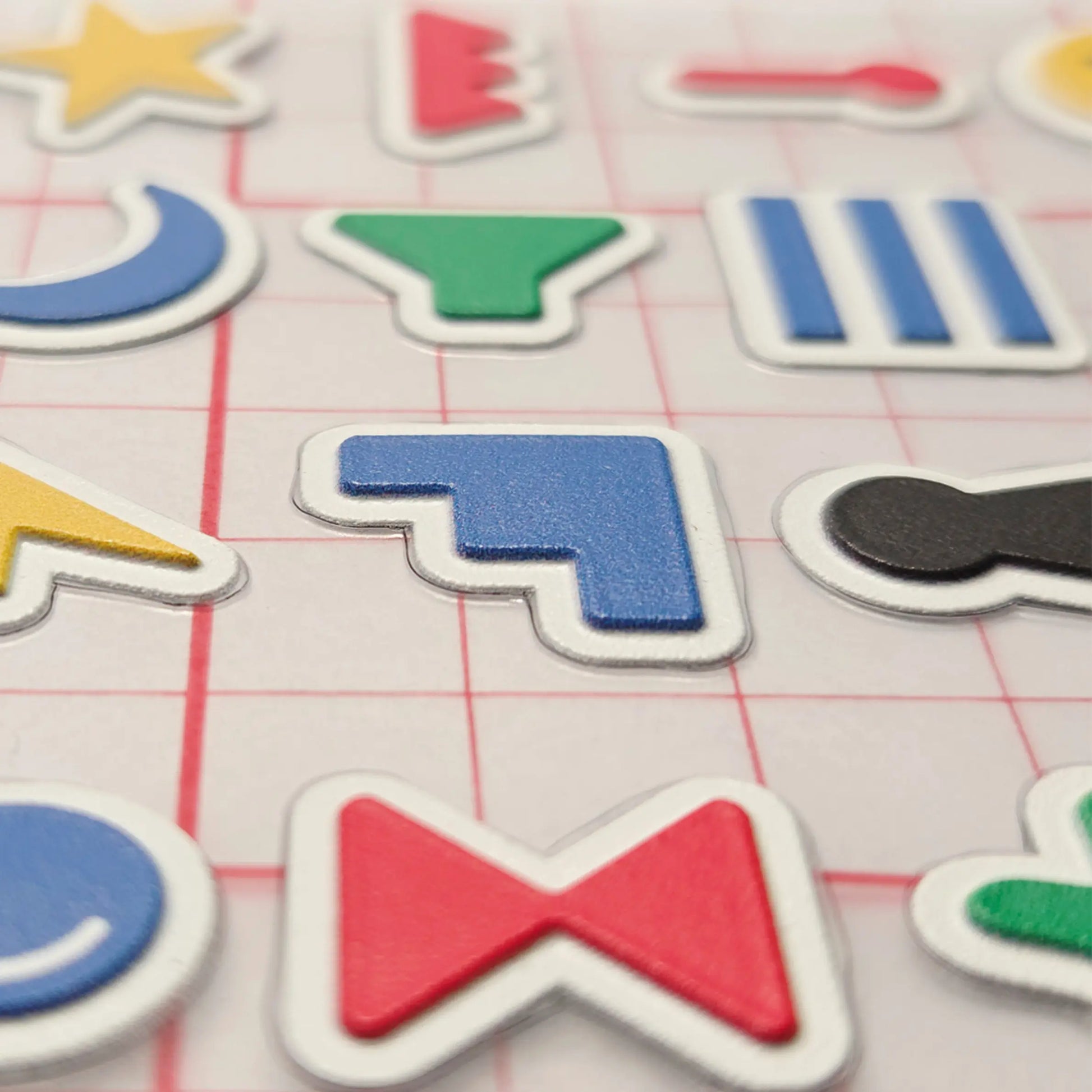 A close-up view of Stactiles icons showing raised, colorful symbols with crisp edges on a transparent grid backing, highlighting their textured, tactile surface.