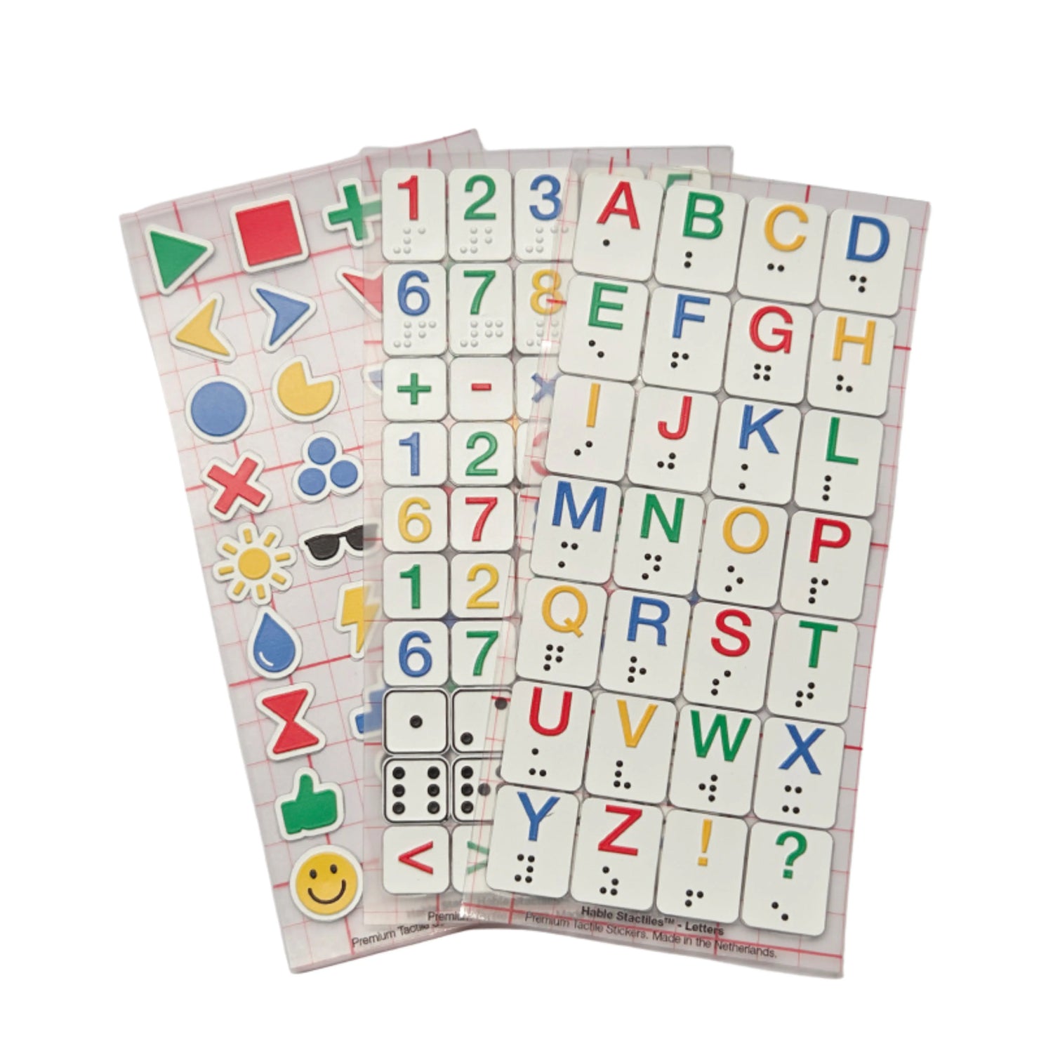 Three Stactiles sheets displayed side by side: one with colorful tactile icons, one with numbers and symbols, and one with raised alphabet letters in different colors. Each sheet features neatly arranged tactile stickers on a transparent grid backing.