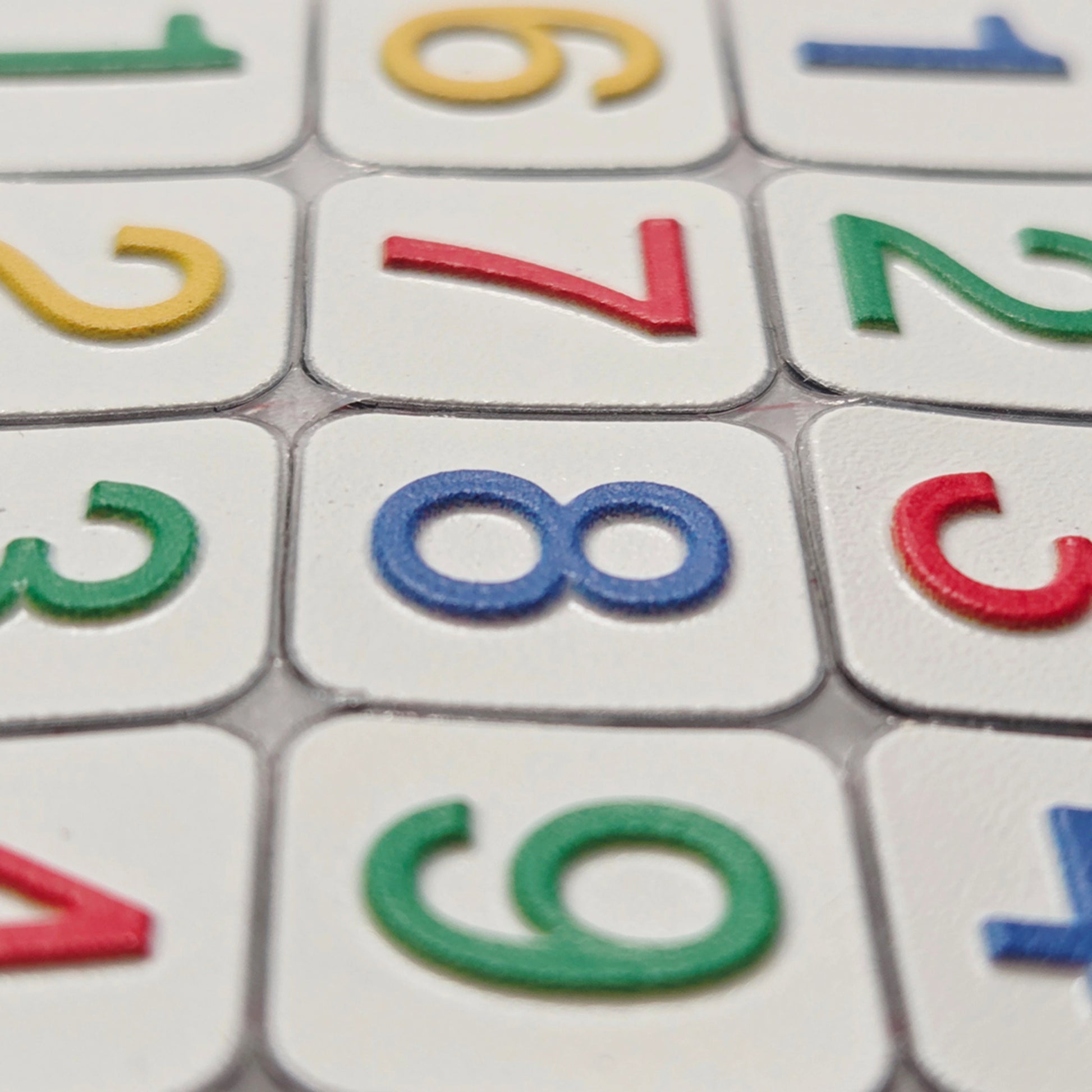 A close-up view of Stactiles Numbers stickers showing raised, colorful digits on white tactile tiles. The texture and height of the embossed numbers are clearly visible in the detailed shot.