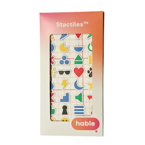 Packaging of the Stactiles Icons Pack by Hable. The front of the box shows a window revealing colorful tactile icons in various shapes, including hearts, triangles, moons, flowers, lightning bolts, sunglasses, and more. The box has a gradient orange-pink top section with the word 'Stactiles™' and a pink bubble with the Hable logo at the bottom.