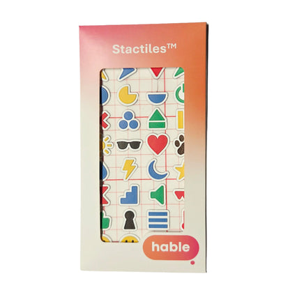 Packaging of the Stactiles Icons Pack by Hable. The front of the box shows a window revealing colorful tactile icons in various shapes, including hearts, triangles, moons, flowers, lightning bolts, sunglasses, and more. The box has a gradient orange-pink top section with the word 'Stactiles™' and a pink bubble with the Hable logo at the bottom.
