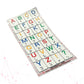 A loose Stactiles Letters sheet showing raised tactile alphabet stickers in bright colors, each with corresponding braille dots beneath the letter. The stickers are arranged in a grid on a transparent backing with a faint red guide grid.