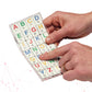 Two hands hold a Stactiles Letters sheet while a finger traces one of the raised, colorful alphabet stickers with braille dots. The tactile letters are arranged in a neat grid on a transparent backing.